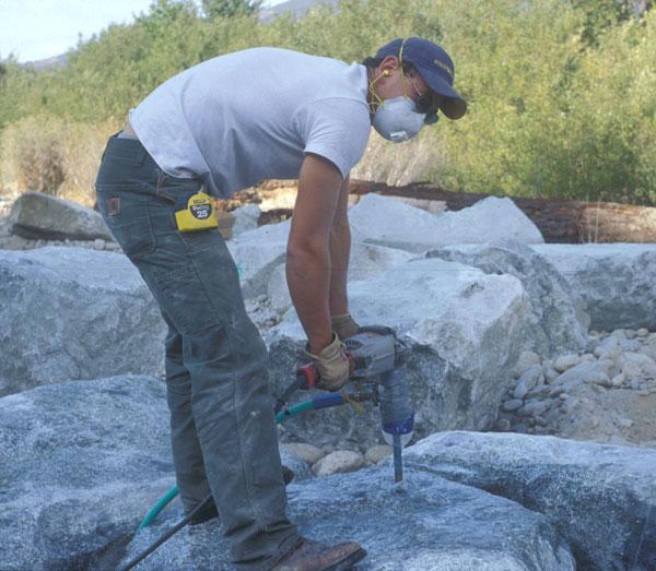 PREPARING BOULDERS Will Drew uses an impact drill to make 7/8-inch holes, which were thoroughly cleaned