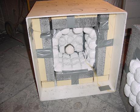 The inner box houses the explosive device. A simple suspended net or a false floor provides centering of the device in the box.