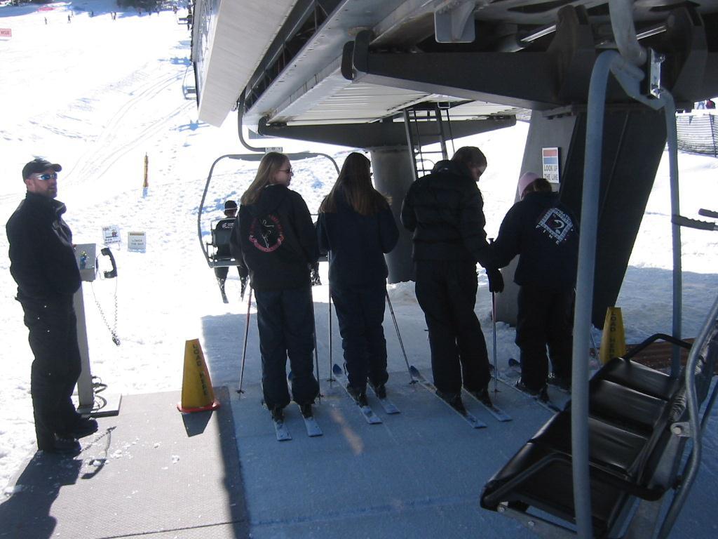 When you have finished reading the signs, and you are comfortable with trying your first chairlift ride, stand on the red, Wait Here line. Remove your pole straps.