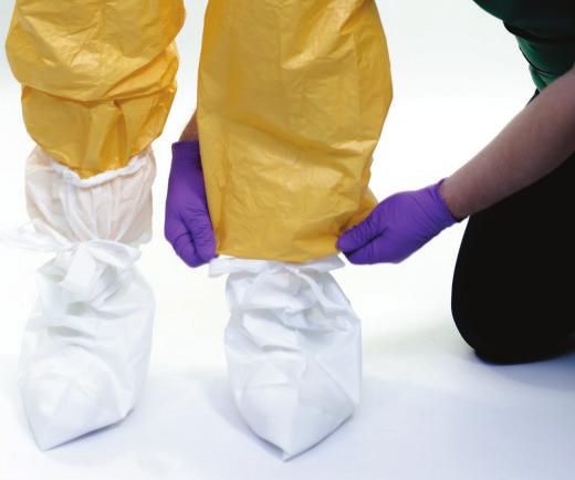 Boot covers covering the clogs. Boot covers are placed outside of PPE user's shoes and the coverall legs; Clogs under boot covers.