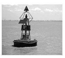 (b) The photograph shows a floating buoy used to warn boats about shallow water. The buoy has a lamp and a bell.