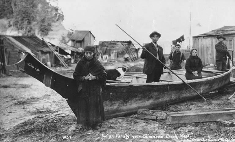 8. Clallam Indians (the Hicks family) pose with canoe near Chimacum Creek, Washington, ca. 1914 Older woman in head scarf & shawl over her shoulders stands at the prow of a beached canoe, ca.
