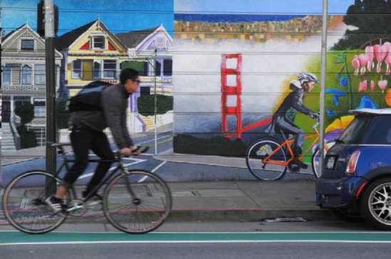 PAGE 77. Image: Cyclist riding in a green bike lane with a mural in the background.