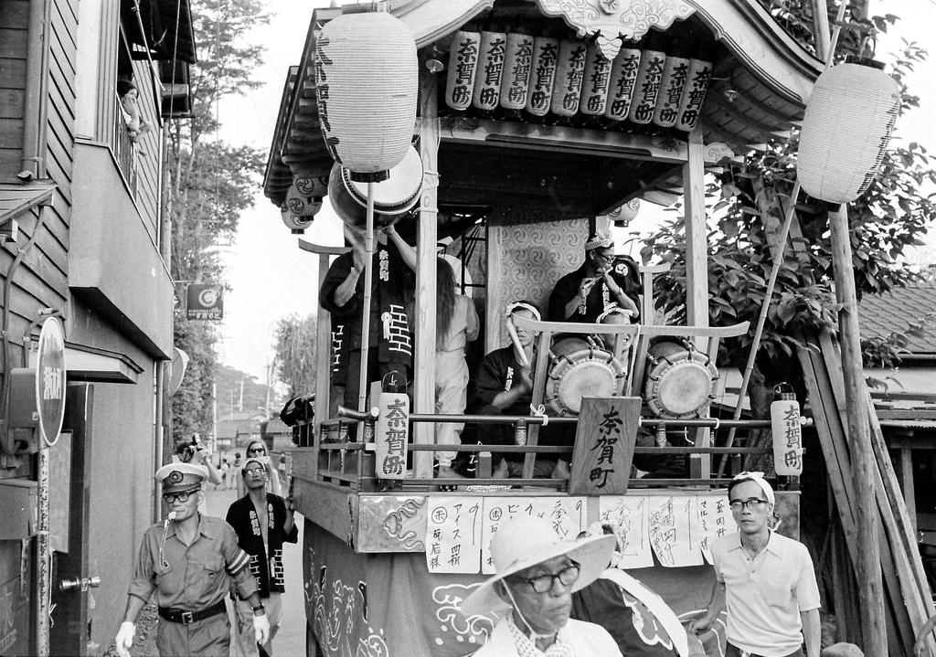 This four-wheeled portable shrine (Dashi) has several people in or on top of the vehicle as well as several others on the ground to guide it through the streets.