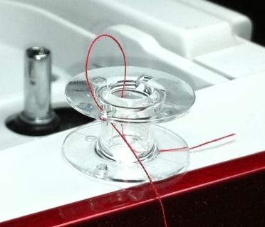 The traditional method of winding a bobbin is to hold the free end of the thread coming out of the hole while winding.