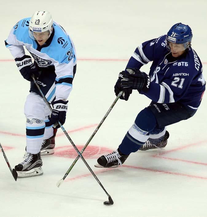 The two players try to get control of the puck. Players move the puck on the ice with a long stick.