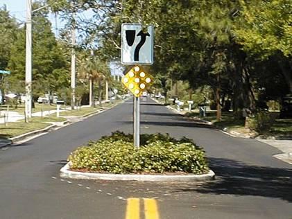 Raised median through intersection. These devices may be used on the centerlines of local and collector roadways to prevent left-turn and through movements to and from intersecting streets.