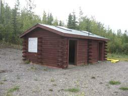 The shelter is built of squared logs that were apparently milled locally at the time of construction. The floor is concrete and the roof is sheet metal.