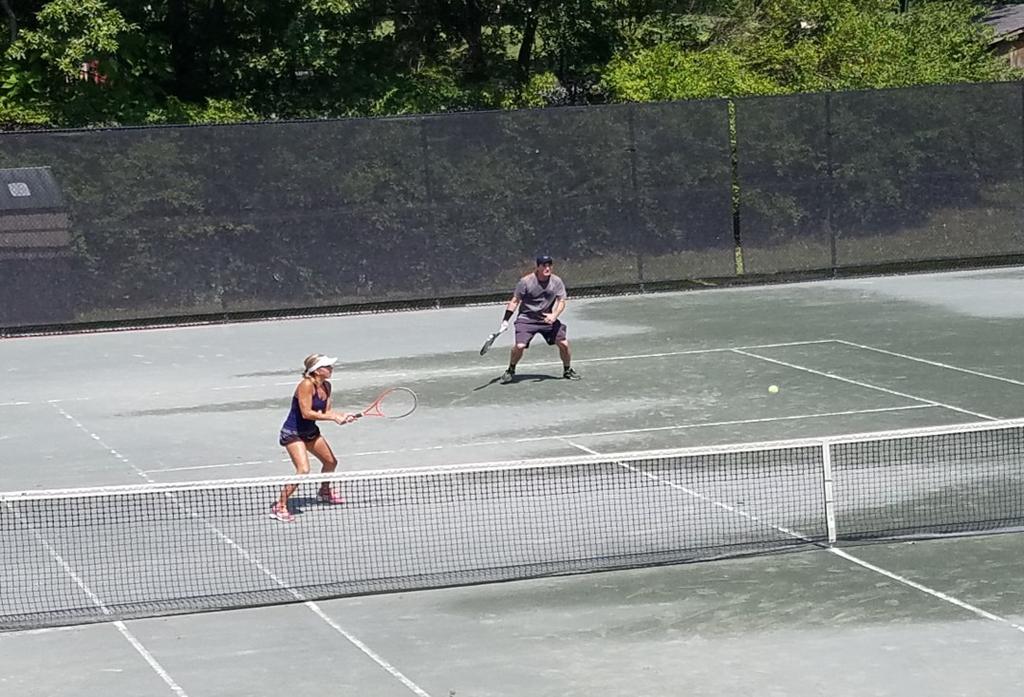 singles match. Rodney Harrison spins a serve in while partner Colleen Sommer gets ready to pick off the volley at the net.