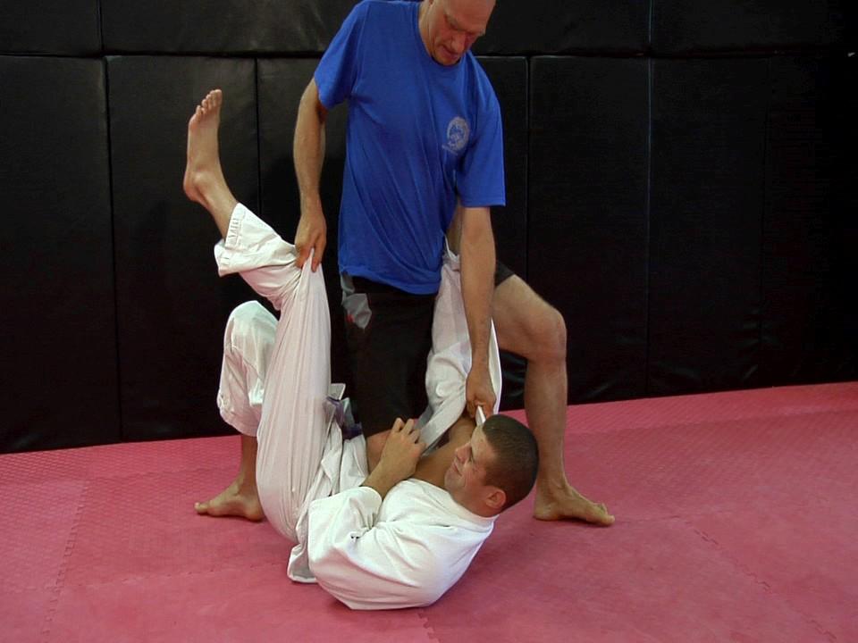 In the Knee Mount with the gi you can pull him towards you with a variety of grips: near collar and near sleeve, or the near collar and far knee, it's all the same.