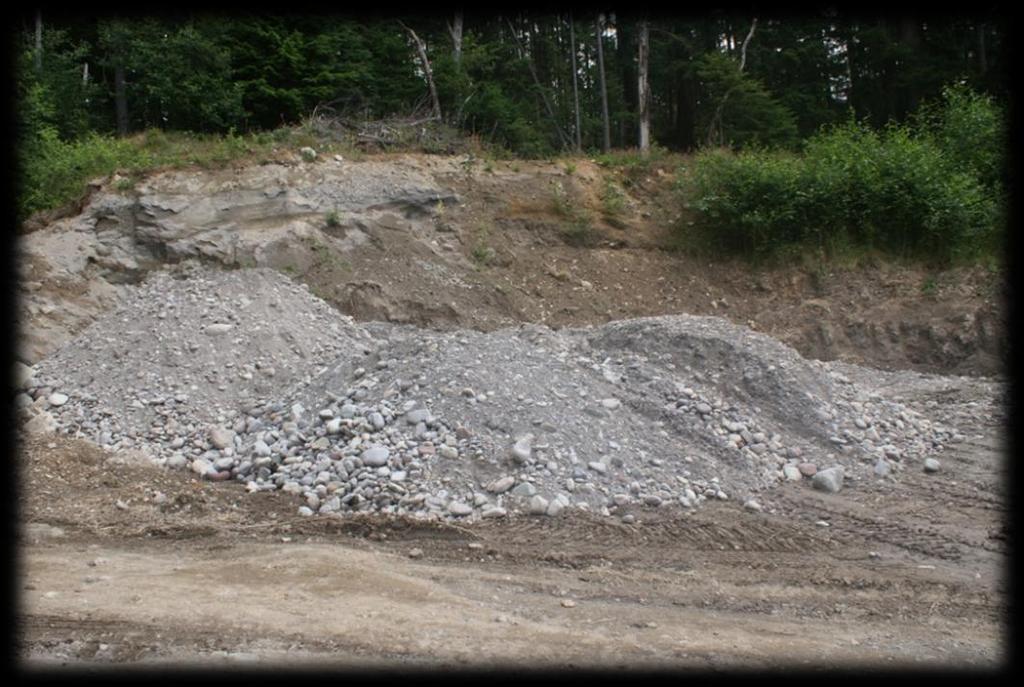 This photograph is taken at the Bowen Island Sand & Gravel Pit. It shows the nine loads of river gravel that were trucked from Squamish to Bowen for storage.