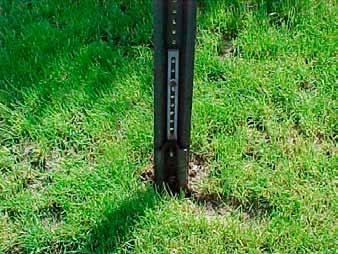 The wood post is inserted and stabilized with steel shim plates, and holes are drilled near the base of the post perpendicular to the flow of traffic to provide a breaking point upon impact.