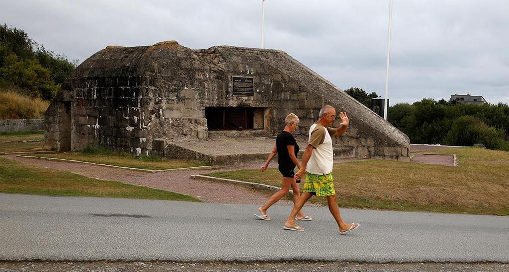 Tourists walk past a former German bunker overlooking the D-Day landing