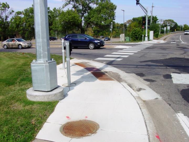 2 meters) at the end of the pedestrian curb ramp. In the example shown the APS button could not be mounted on the signal pole and the required pedestrian push button station was installed.