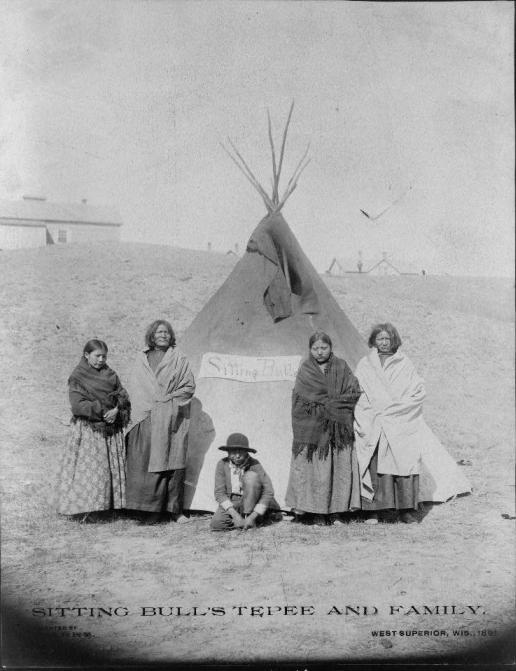 Barry & Assistant #2 Sitting Bull's family in front of the log house at Grand River Left to right: unknown, Lodge In Sight, Four