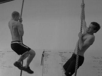 Two students climb vertical ropes in the gym. Each of them has a mass of 70 kilograms.