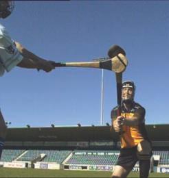 As the opponent throws the sliotar up, bend into the tackle as if lunging.