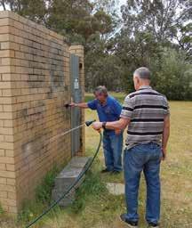 Graeme Whitehead scrubs while Bill Dunne hoses the wall down in the course of removing the graffiti.
